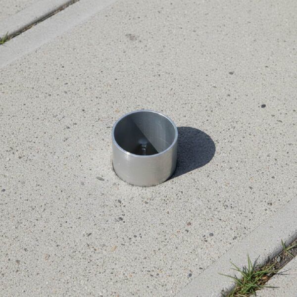 Eine Einbetonierte Bodenhülse, welche ca. 5cm aus dem Beton Herausragt.