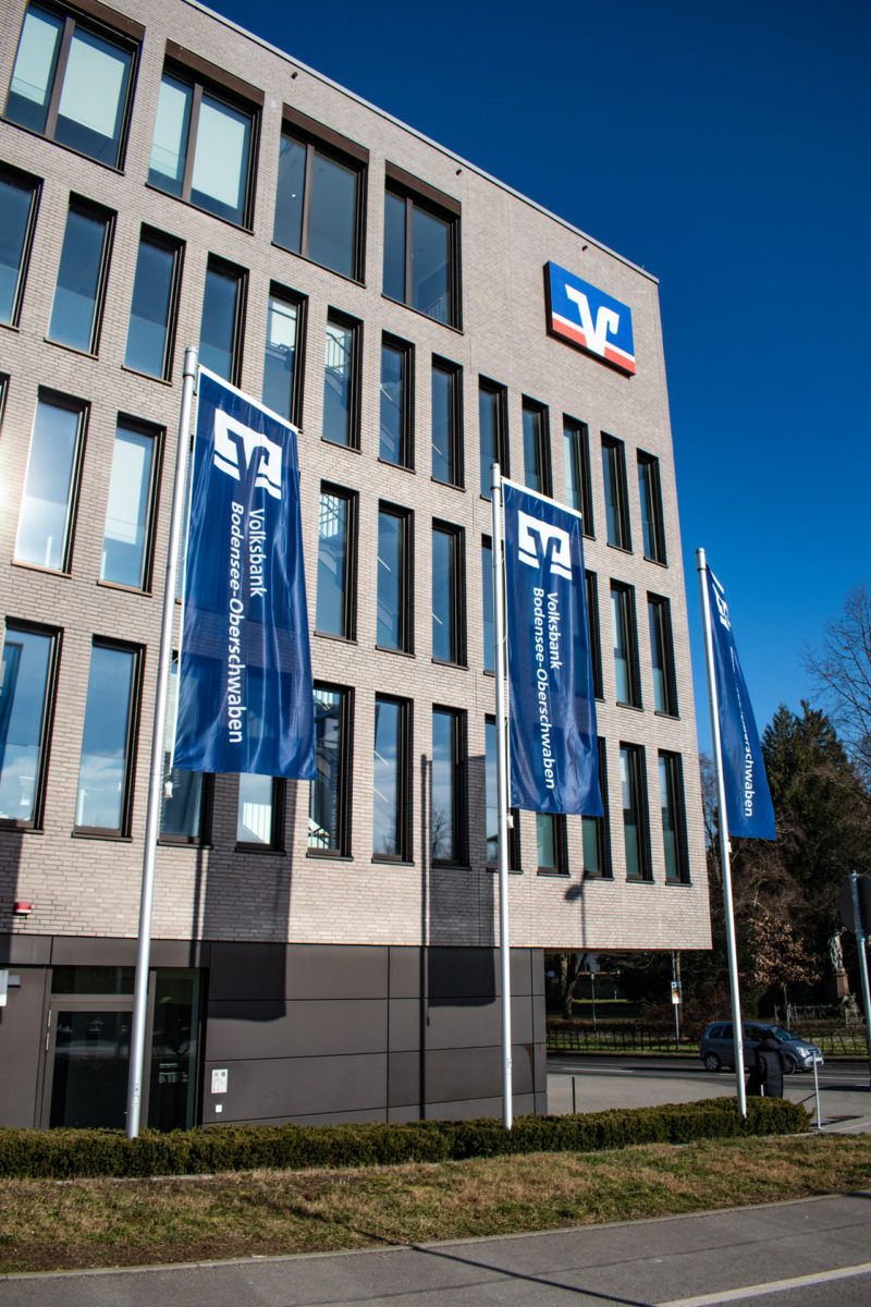 Volksbank Ravensburg mit drei blauen Fahnen auf hohen Fahnenmasten vor der Firmenzentrale